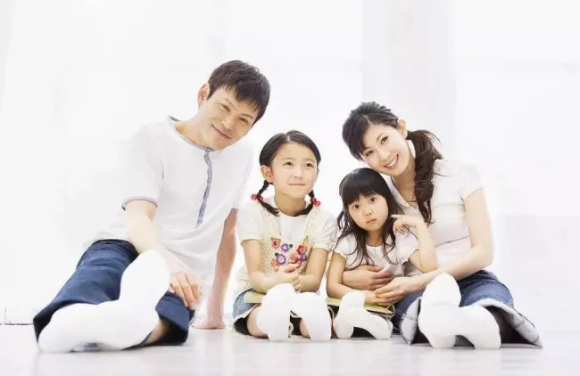 Smiling family of four sitting on the floor in a bright room.